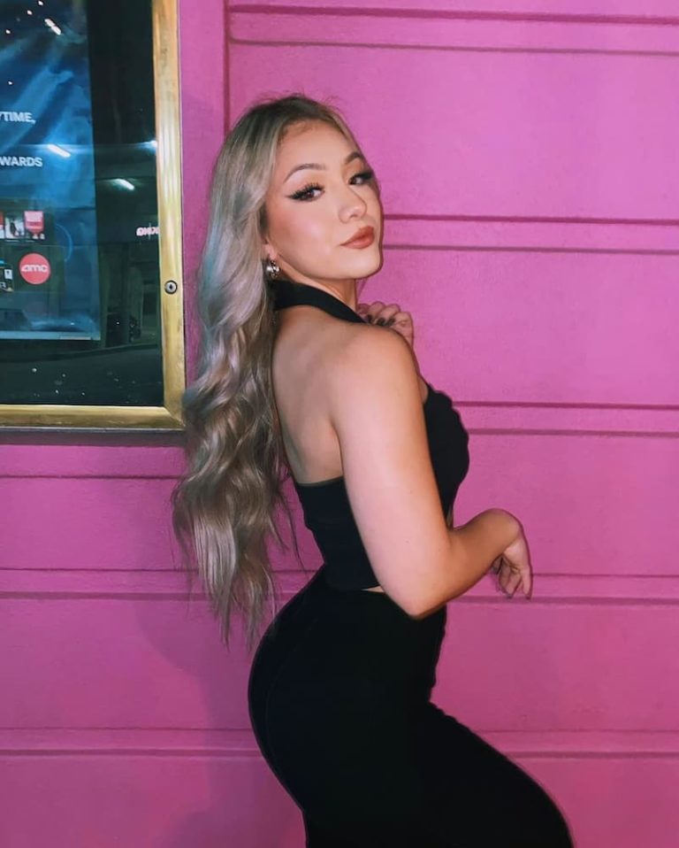 close up of woman in black dress in front of pink wall