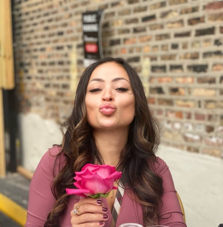 mujer sosteniendo una flor posando frente a una pared de ladrillos