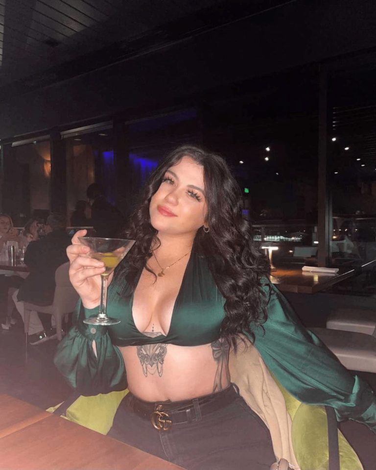 woman in dark green top posing with drink in hand