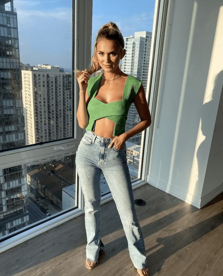 woman posing in green top and jeans in front of cityscape background