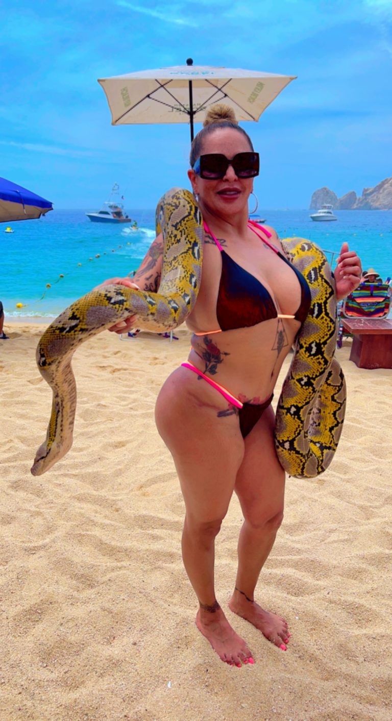 woman in black and pink swimsuit smiling in front of beach