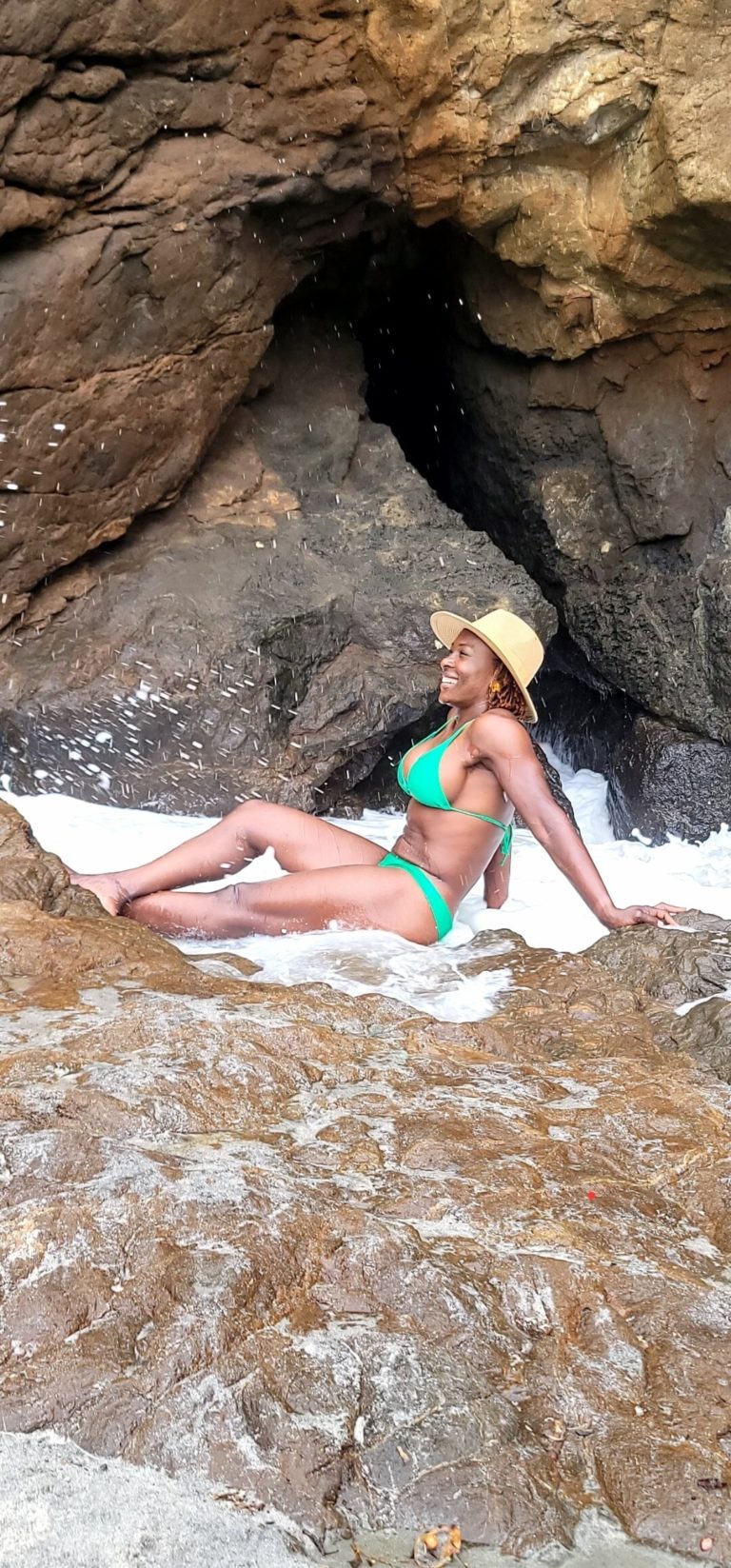 woman in green swimsuit posing in front of cave